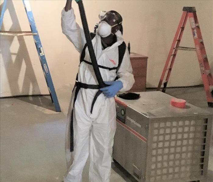 servpro employee in white protective gear cleaning basement