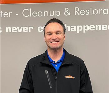 smiling man with brown hair and a black Servpro jacket on