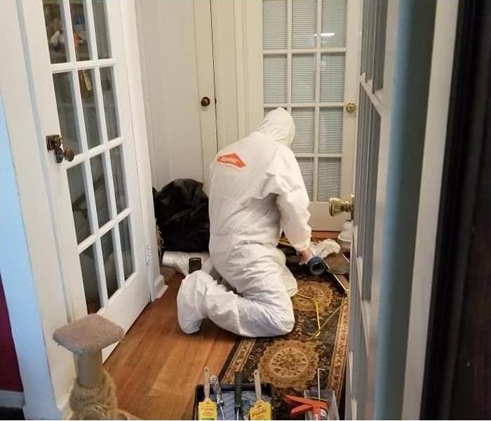 Man in protective clothing with SERVPRO logo kneeling on a hallway floor